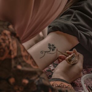 A close-up of an intricate henna tattoo being applied on an arm by an artist.