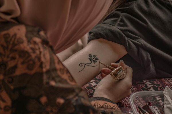 A close-up of an intricate henna tattoo being applied on an arm by an artist.