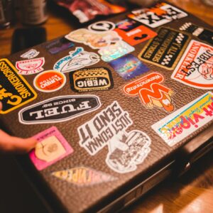 A suitcase covered with various colorful stickers on a wooden table indoors.