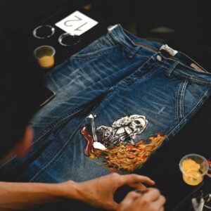 Close-up of artist painting a unique design on blue denim jeans with vibrant colors.