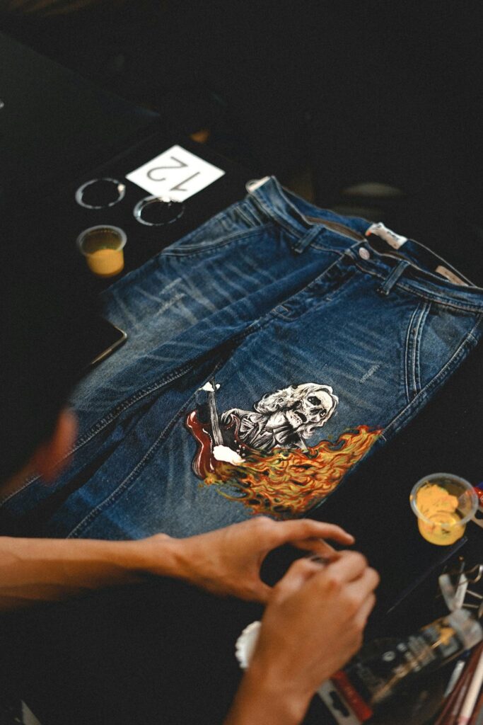 Close-up of artist painting a unique design on blue denim jeans with vibrant colors.