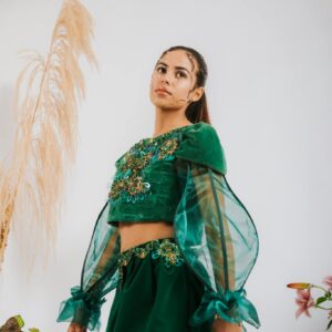 Woman in a stylish green traditional outfit posing indoors with elegant decor.